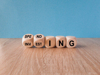 Spending or investing symbol. Turned wooden cubes and changes the word investing to spending. Beautiful wooden table, blue background, copy space. Business and spending or investing concept.