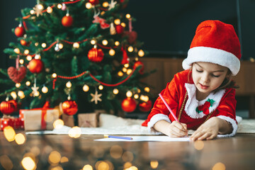 Little girl writing her letter to Santa near the beautifully decorated New Year tree