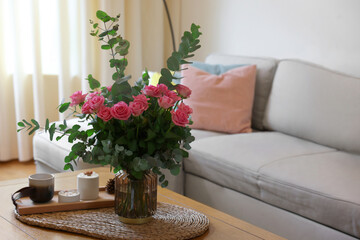Fototapeta na wymiar Beautiful bouquet of roses and eucalyptus branches in vase near candles on table at home. Space for text