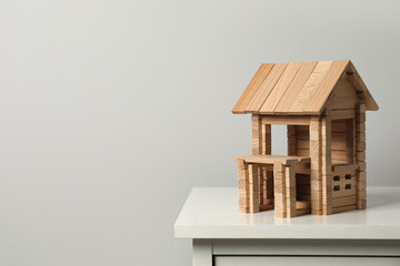 Wooden house on chest of drawers near light grey wall, space for text. Children's toy