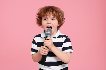 Cute little boy with microphone singing on pink background