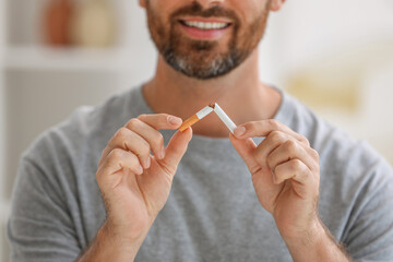 Stop smoking concept. Man breaking cigarette on blurred background, closeup