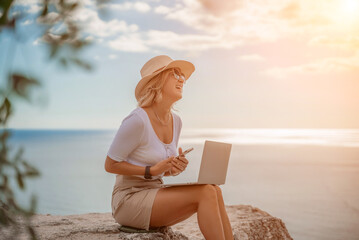 Freelance women sea working on the computer. Good looking middle aged woman typing on a laptop keyboard outdoors with a beautiful sea view. The concept of remote work.