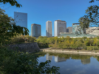 Fototapeta premium Promenade and trails inside public park in Japanese city of Osaka with modern architecture skyline cityscape view and historic fortress nature landscape scenery lots of trees, plants and bushes autumn