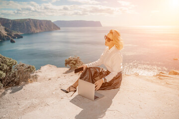 Freelance women sea working on a computer. Pretty middle aged woman with computer and phone outdoors with beautiful sea view. The concept of remote work.