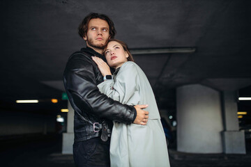 young couple in love hugging on a date in a leather jacket and raincoat in an underground parking lot. Relationship concept