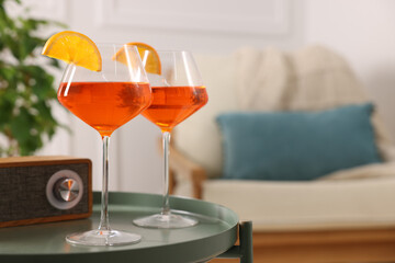 Tasty cocktail in glasses with orange slices and radio set on table in room, space for text. Relax at home