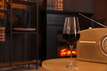 Glass of red wine and retro radio receiver on table in room, space for text. Relax at home