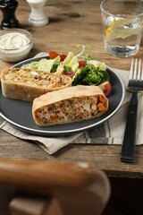 Pieces of tasty strudel with chicken, vegetables and salad on wooden table