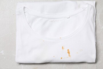 Dirty t-shirt with stains of sauce on light grey marble table, top view