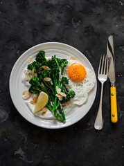 Grilled broccolini with greek yogurt and toasted almonds and fried egg on a dark background. Delicious breakfast, brunch