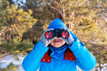 Happy smiling Woman in blue jacket looking through binoculars at birds in coniferous winter forest Birdwatching, zoology, ecology Research in nature, observation of animals Ornithology