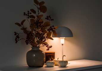Autumn bouquet in a vase, pumpkins, a table lamp on the table in the evening living room