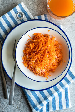 Overhead view of a bowl of grated carrot and a glass of juice