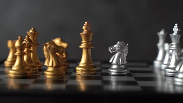 Concept of leadership. Golden chess king faces horse knight on board on white background. Abstract image showing business leadership with camera panning to the right.
