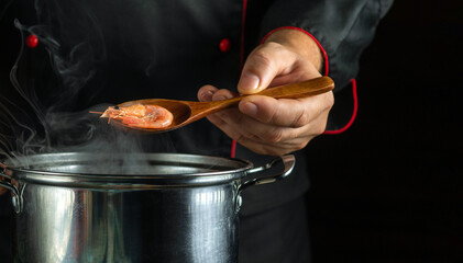 Professional chef prepares delicious shrimp in a pan in the kitchen. The concept of a delicious scampi lunch for a restaurant. Spoon in the cook dinner wis prawn - obrazy, fototapety, plakaty