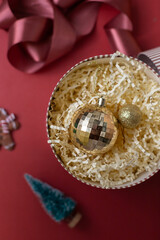 Christmas decorations in the round gift box with fir tree on the red background. Close up winter holidays greeting card.