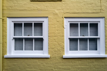 Fototapeta na wymiar Abstract view of a pair of sash wooden windows seen on a painted yellow seaside house in the UK.