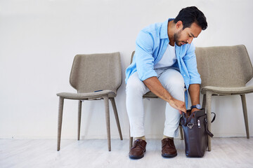 Man, interview and job in waiting room, chair and looking for cv in bag by wall background. Business person, recruitment and marketing opportunity or vacancy, human resources and hiring for position