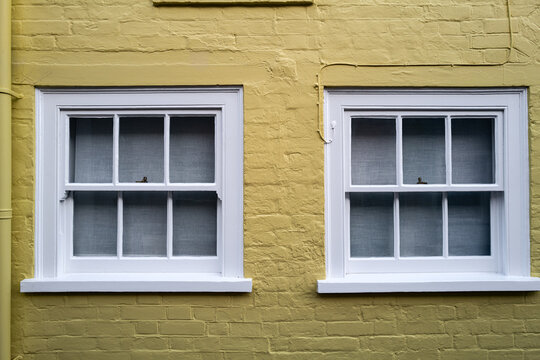 Abstract view of a pair of sash wooden windows seen on a painted yellow seaside house in the UK.