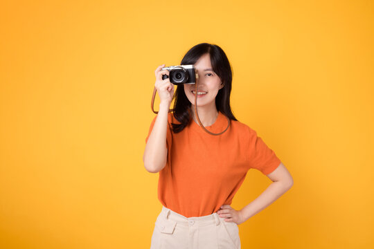 Vibrant young asian woman with camera isolated on yellow background, showing the adventure of exploring new places on vacation.