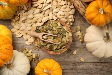 Many fresh pumpkins and seeds on wooden table, flat lay