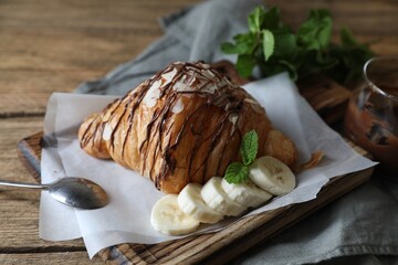 Delicious croissant with chocolate, banana and spoon on wooden table