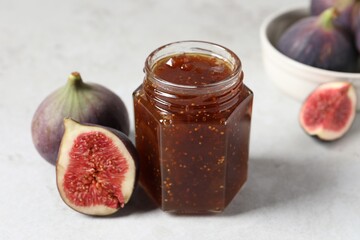 Jar of tasty sweet jam and fresh figs on white table, closeup