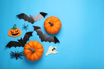 Flat lay composition with cardboard bats, pumpkins, ghost and spiders on light blue background, space for text. Halloween celebration