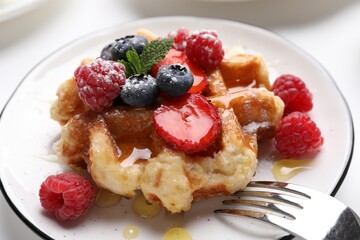 Delicious Belgian waffle with fresh berries and honey on table, closeup