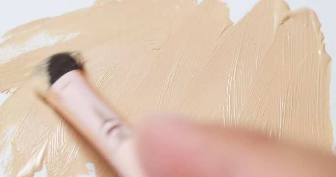 Brushing a nude colored concealer on a clean, white board using a small wand applicator.