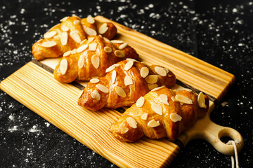 Almond Croissant topping with nuts served on wooden board side view of french breakfast baked food item