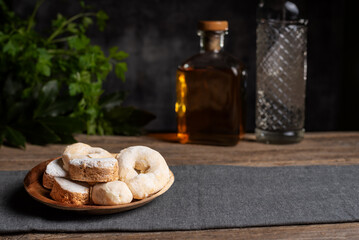 Shortbread, wine donuts and puff pastry on a wooden plate, and in the background and out of focus some bottles of anise and typical Christmas liqueur. Christmas concept.