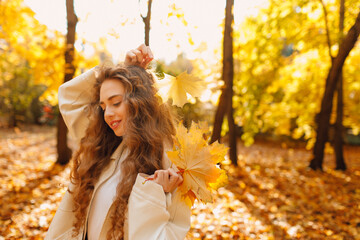 Smiling young woman holds yellow leaf in her hand in the park at sunset