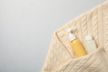 Cosmetic bottles in sweater on white background, space for text