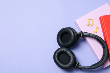Headphones and books on purple background, space for text