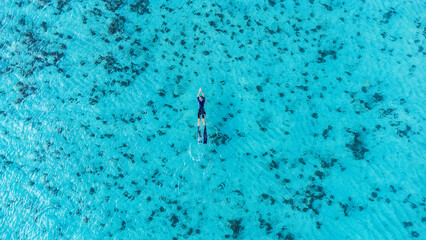 Stunning aerial view of a young woman swimming with carbon fins and wetsuit in turquoise waters...