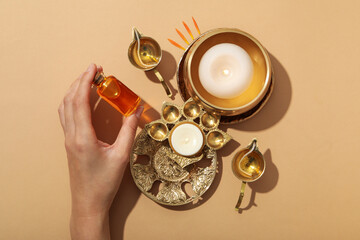 Copper oriental utensils, bottle of oil in hand and candles on beige background, top view