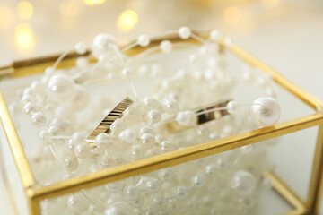 Wedding rings in jewelry box with pearls on light background, close up