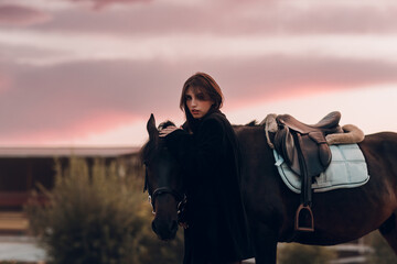 Young woman in black with her horse at sunset outdoors