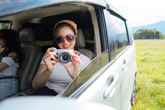 beautiful female smiling friends going on a trip while sticking head out of car in motion to see the view and take photos