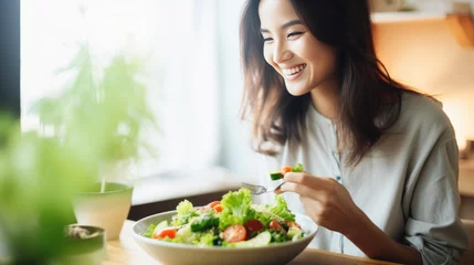 Fotobehang Young athletic woman eats a salad in her plate while eating breakfast © MP Studio