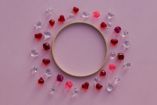Glass hearts and polyhedra, round wooden frame on pink background