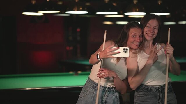 two women take pictures with a smartphone. Caucasian women play billiards. women relax together. slow motion video. Record high quality video in Full HD format.