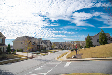 Three-way road intersection with stop sign, row new development suburban two story houses along street leading down steep hill near Atlanta, Georgia, USA, well-trimmed landscape - obrazy, fototapety, plakaty