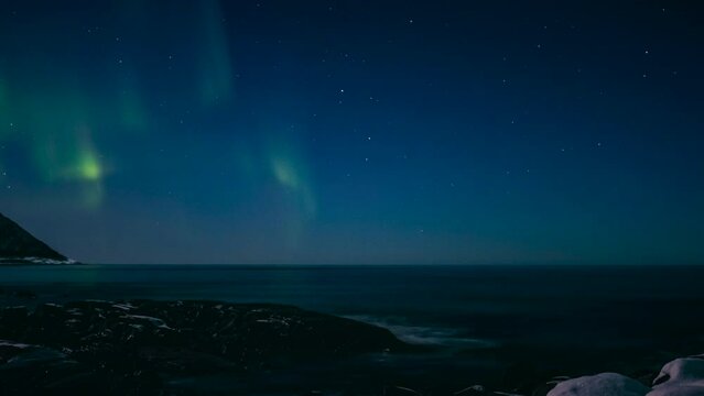 Northern Lights polar light or Aurora Borealis in the night sky over Senja island in Northern Norway time lapse. Snow covered mountains in the background with water of the Norwegian Sea reflecting the