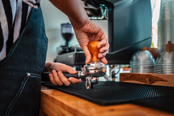 Barista cafe making coffee with manual presses ground coffee using a tamper at the coffee shop