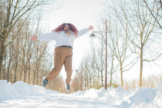 Smiling plump redhead woman jumping in park in winter. 