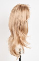 Fototapeta premium Natural looking blonde wig on white mannequin head. Long hair on the plastic wig holder isolated on white background, side view.