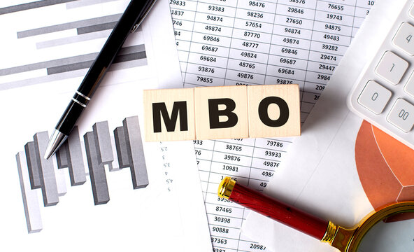 MBO text on wooden block on graph background with pen and magnifier